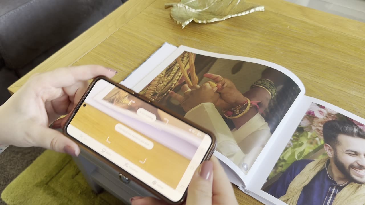 A phone held over an open Nokoru book, playing the video behind a printed wedding photo